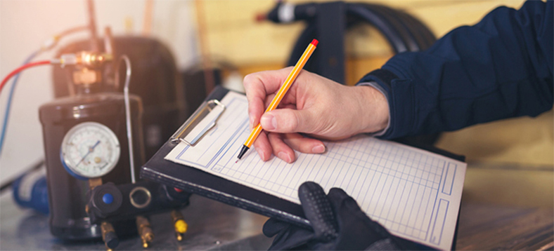 Air conditioning technician recording observations on clipboard with a pencil and wearing a glove on one hand.