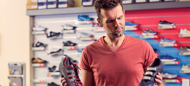A man holding two sneakers and deciding on which one to purchase.