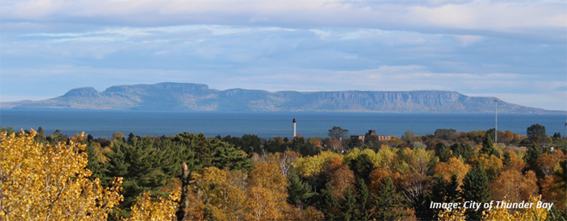 Photo of Thunder Bay with trees in the foreground and the bay with a lighthouse