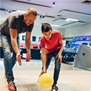 An adult and kid with bowling ball on a bowling alley