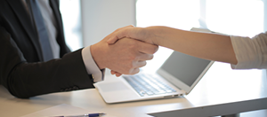 two hands handshaking in front of a laptop