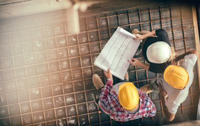 three construction workers with hard hats crowded around a layout plan in a construction zone
