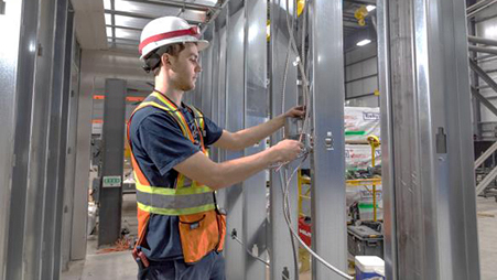 construction worker feeding a conduit through a modular construction facility