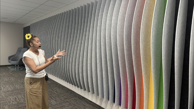 Manon Gagne, Director of Operations, showing the sound-deadening accent wall made from recycled felt material, showcasing its customizability in shape and design, along with the full color spectrum.