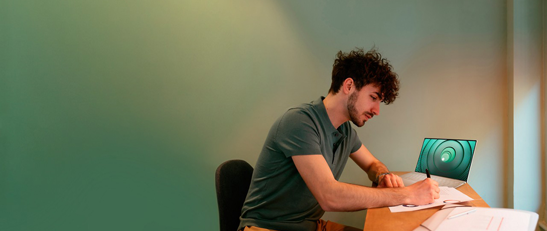 person-sitting-at-a-desk-with-laptop-writing-something-down