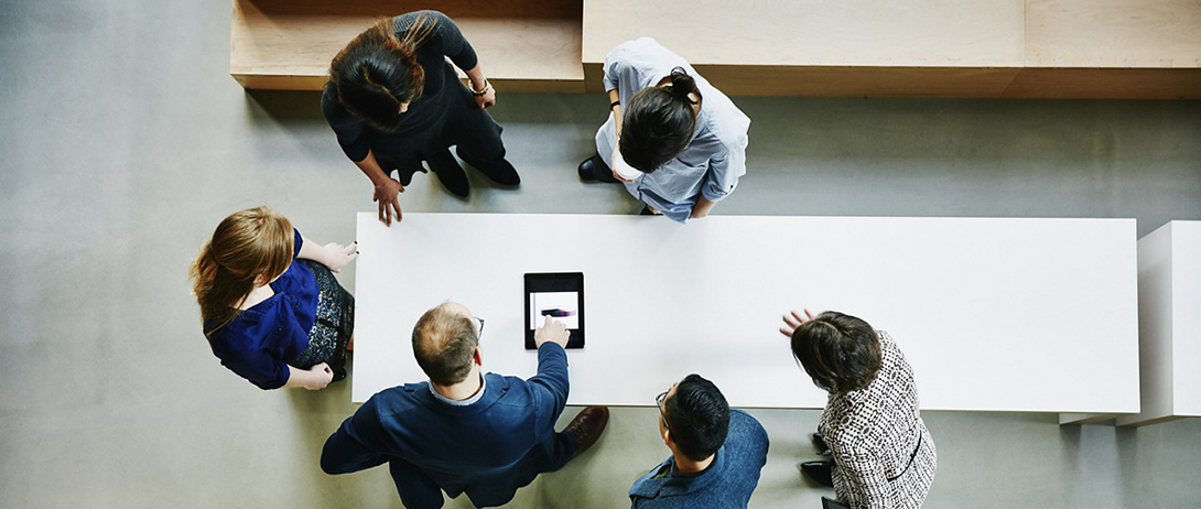 people-crowd-a-table-looking-at-content-on-a-tablet