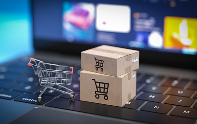 miniature shopping cart along with two boxed packages resting on a laptop keyboard