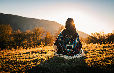 indigenous woman sitting in an open field overlooking a mountain landscape