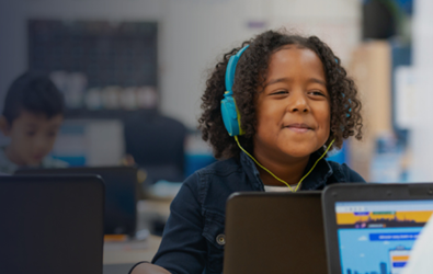 A child with headphones listening through a laptop