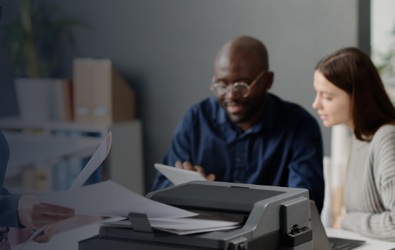 a man on a tablet device showing a woman how to send a print job to a printer