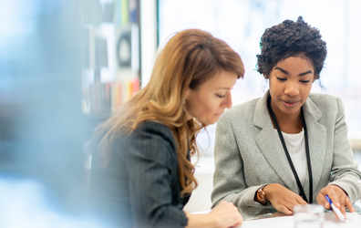 Two women at a table consulting with one another and reviewing