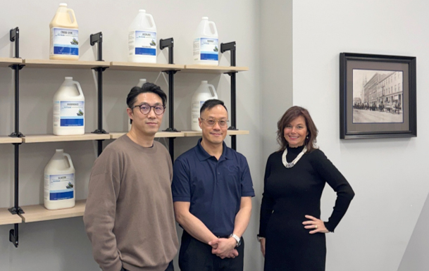 OECM’s Ambrose Lee (Marketing Manager) and Ronald Wai (Category Manager, Supplier Relationship Management) along with Dustbane’s Shannon Hall (Executive Vice President of Sales and Marketing) standing beside shelves of Dustbane cleaning products during OECM’s facility visit