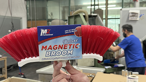Close-up of M2 magnetic broom head held in front of manufacturing equipment