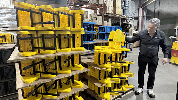 Michael showing stacks of yellow mop buckets and wringers stored in a warehouse