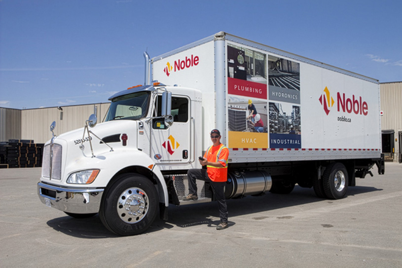 Noble delivery driver standing beside a Noble delivery truck outside their distribution facility.